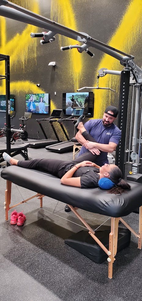 Shawn Taylor giving an assisted leg stretch to a female client lying on a table in a gym