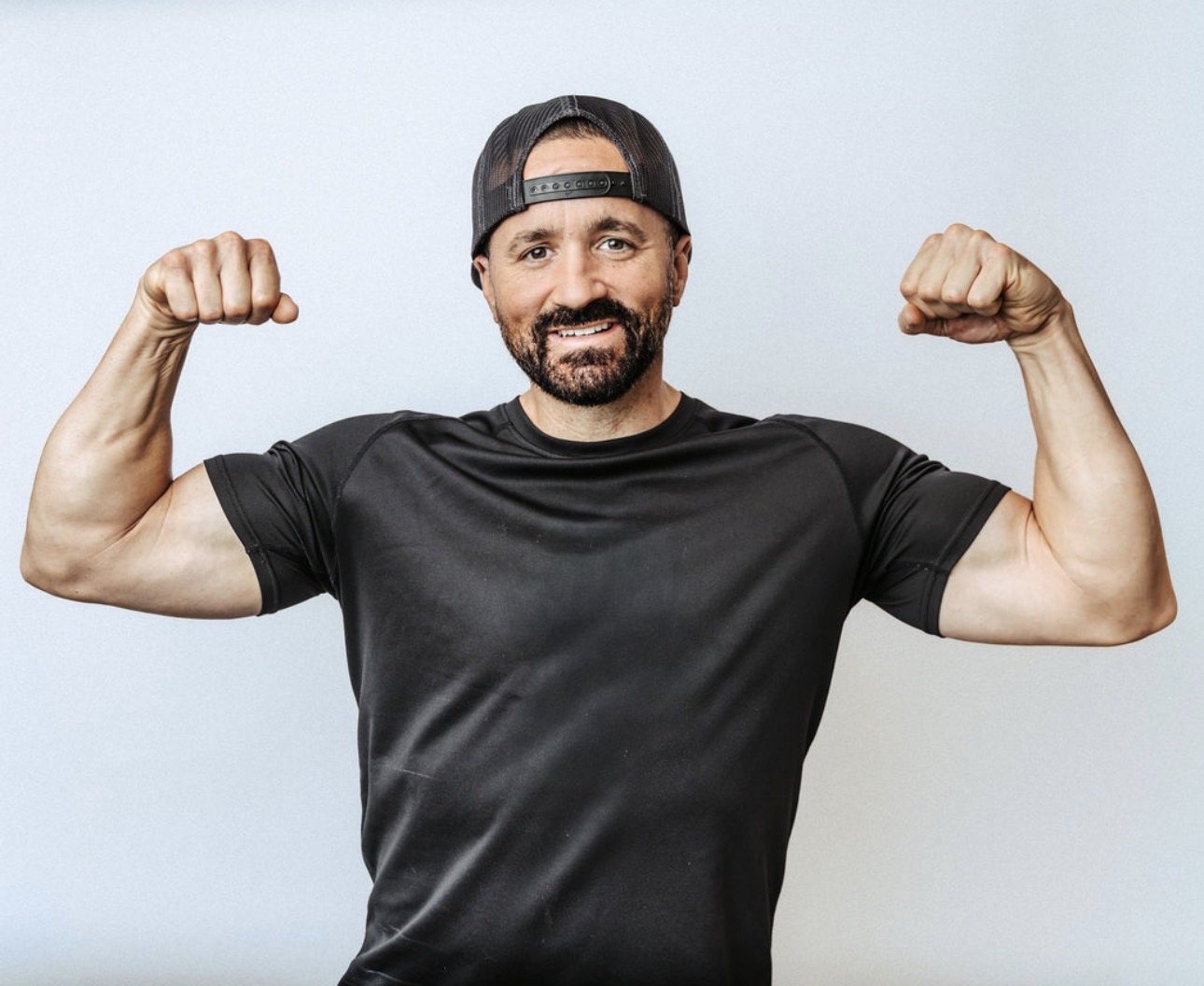 Shawn Taylor flexing both arms and smiling in a bright studio