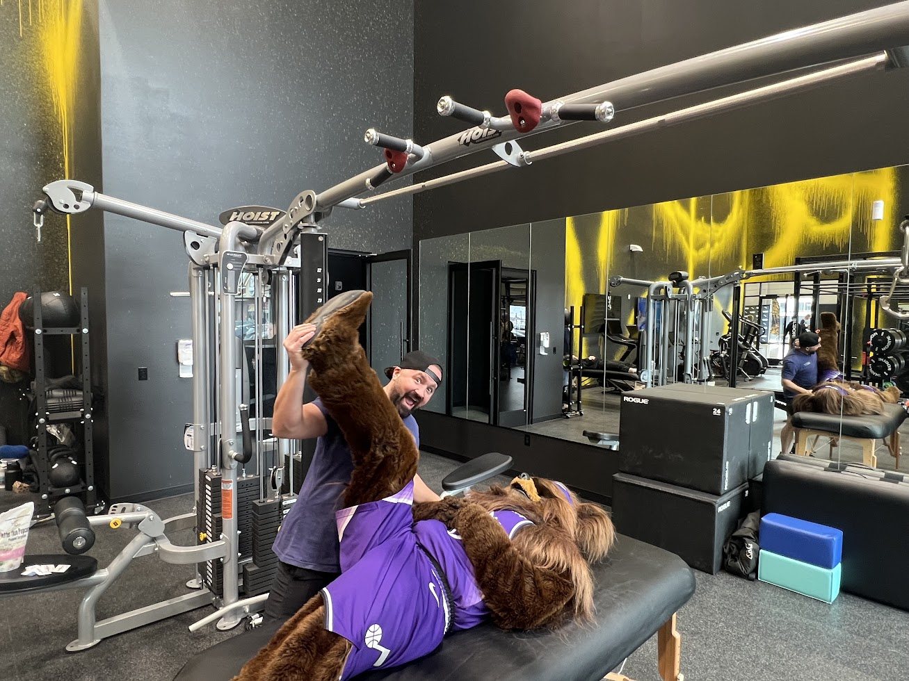 Shawn Taylor giving an assisted leg stretch to a team mascot on a table in a gym